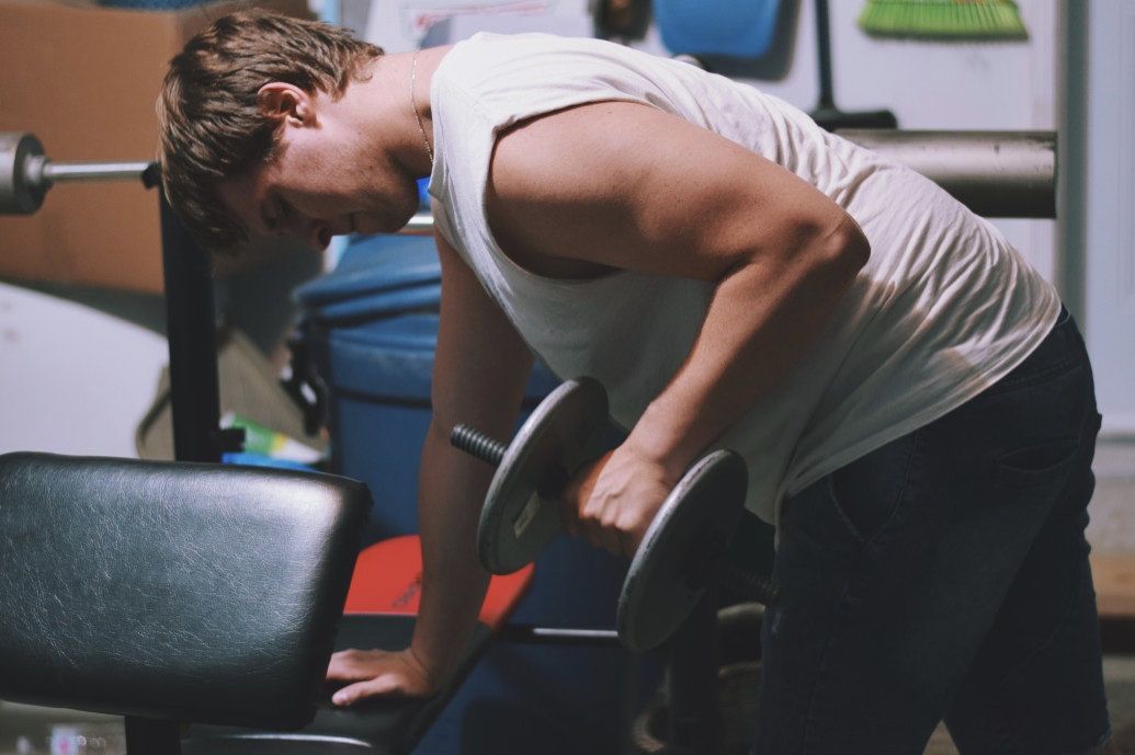 Man leaning over workout bench lifting weight for arm exercise