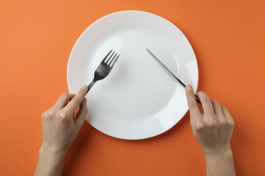 Female hands hold cutlery over the empty plate on orange background