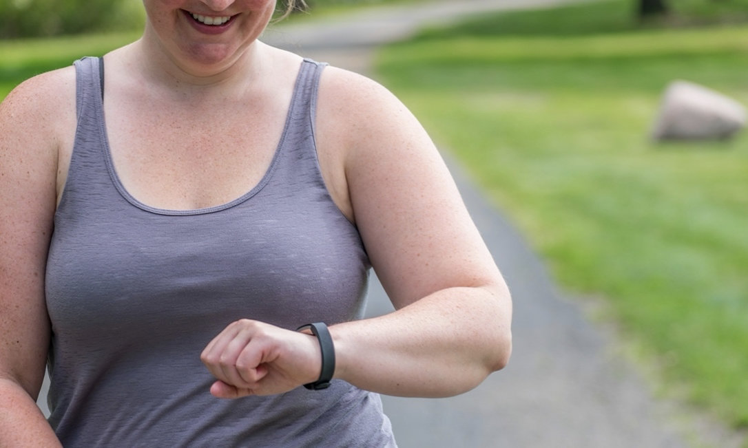 Young woman walking on a path outdoors and tracking exercise fitness on smart watch