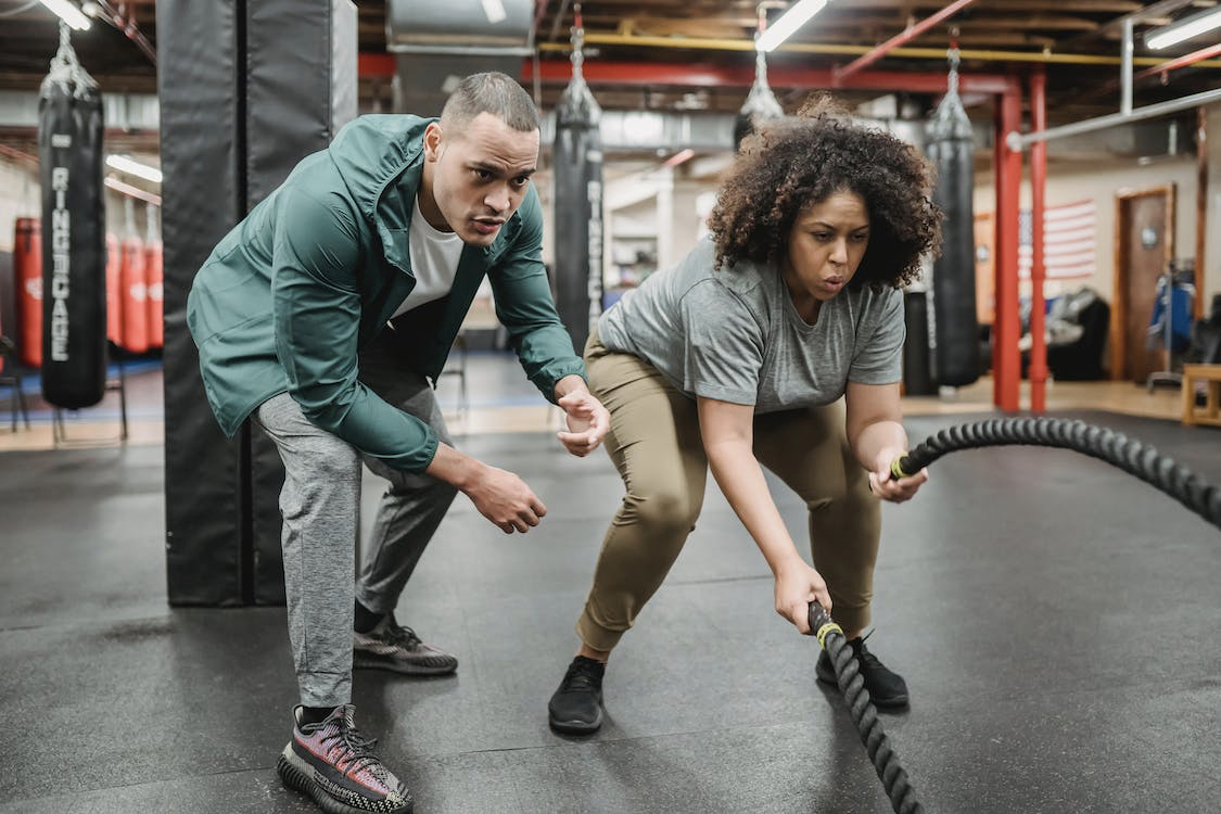 Woman training with ropes and being coached by personal trainer